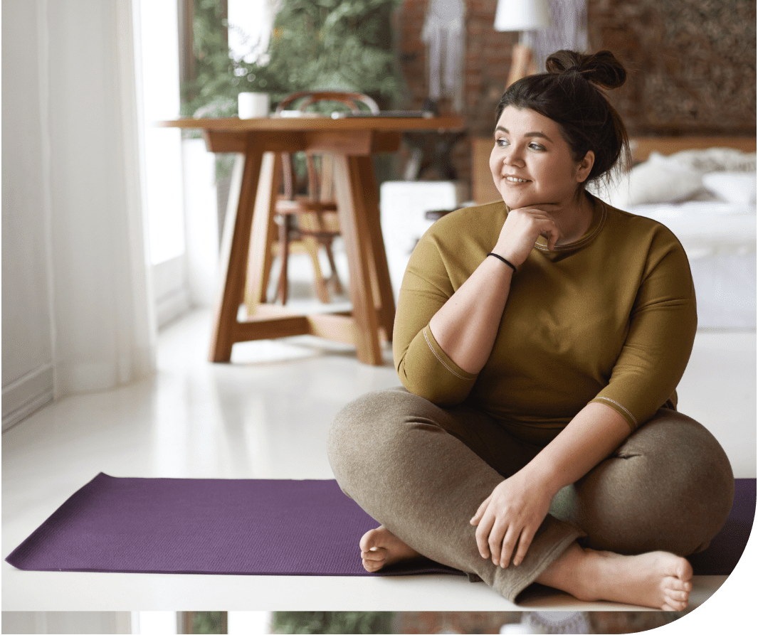 A woman sitting on the ground in front of a yoga mat.